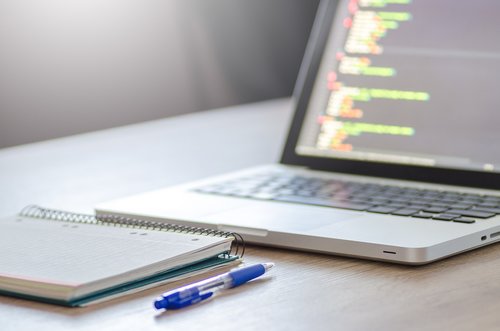 Laptop, spiral notebook, and pen arranged on a desk